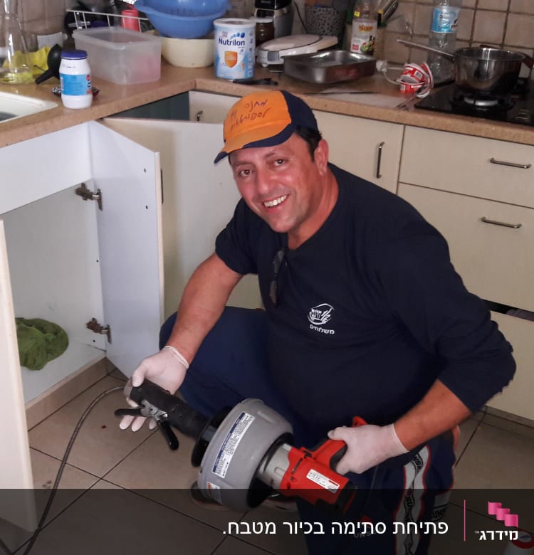 אינסטלטור מחזיק כלי עבודה ליד ארון מטבח פתוח
